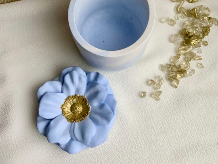 Blauer Gipsbehälter aus zwei Teilen, Deckel in Blumenform mit goldener Mitte.