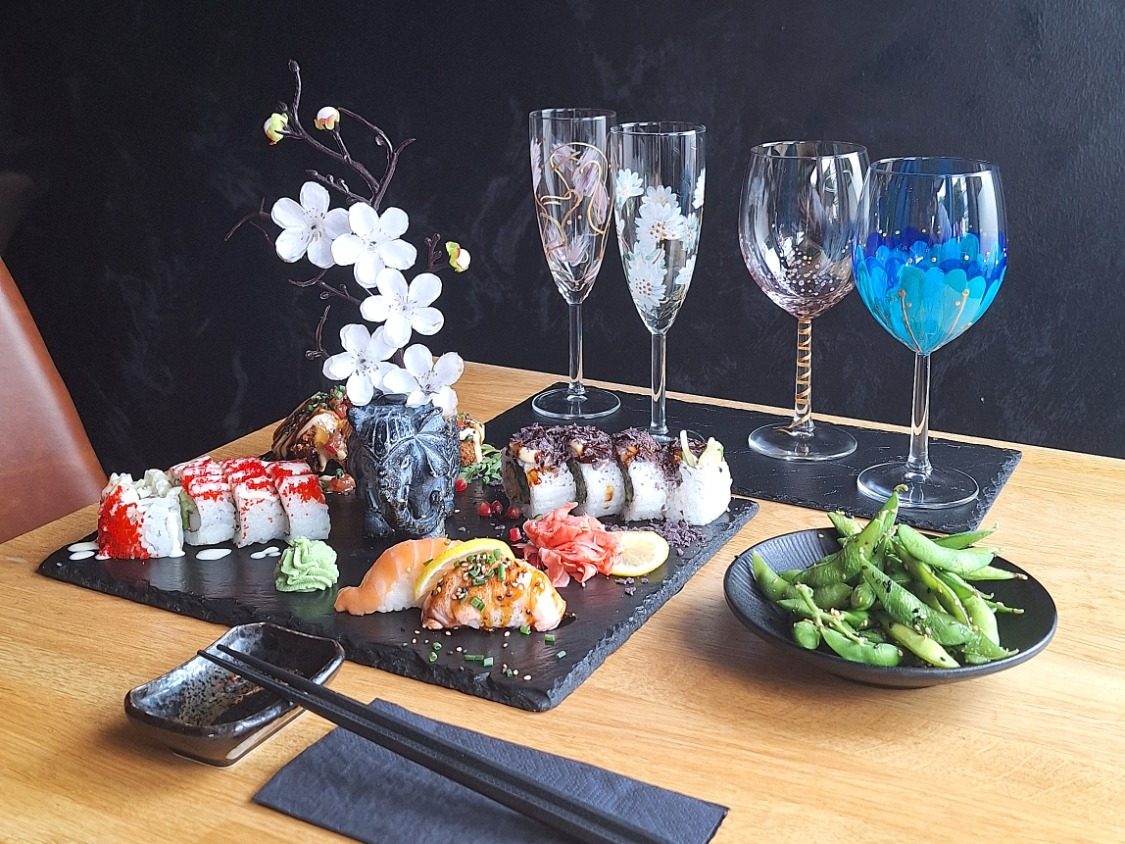 Zwei Hände stoßen mit Wein und Prosecco an, auf dem Tisch italienische Antipasti und Malpinsel.