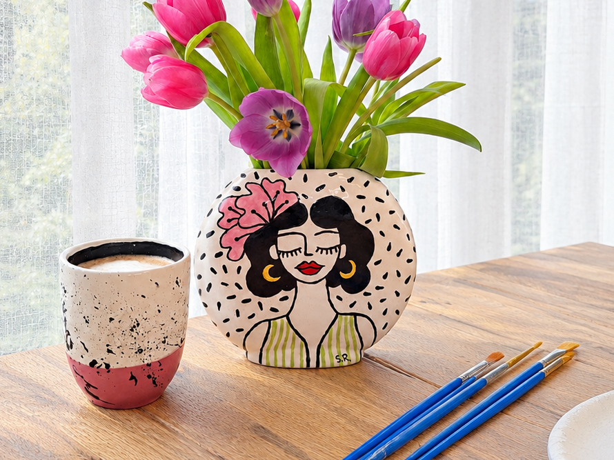 Drei handbemalte Keramikobjekte – Vase, Tasse und Teller – mit Pinseln beim kreativen Malworkshop